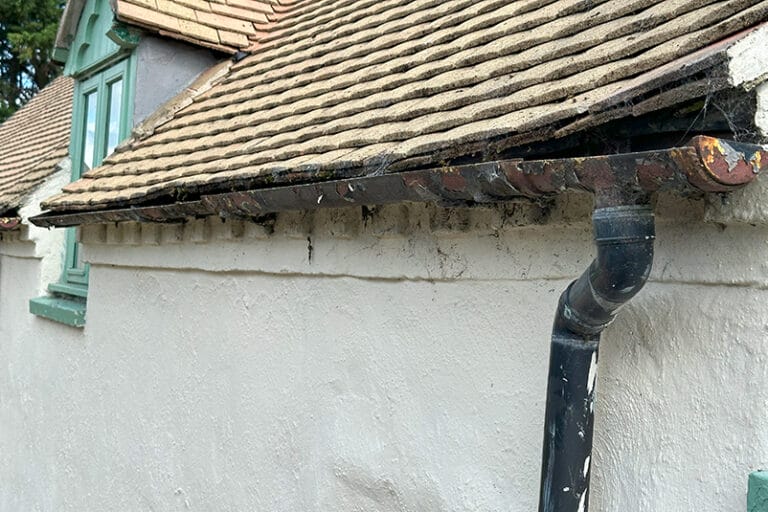 Blocked gutter overflowing with water on an older UK home, showing one of the most common gutter problems in older UK homes